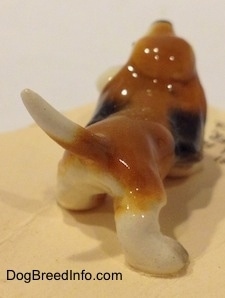 The back of a tan with black and white ceramic Basset Hound figurine that has its front left paw in the air. The tail of the figurine is arched up. 