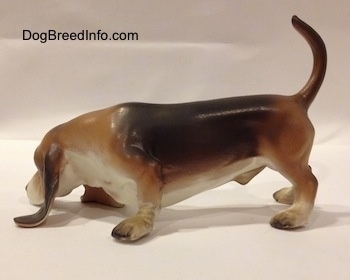 The left side of a brown and black with white porcelain Basset Hound figurine that is sniffing. The tail of the figurine is arched up.