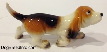 The right side of a black, tan and white ceramic Basset Hound figurine. It is hard to differentiate the ears of the figurine from the body.