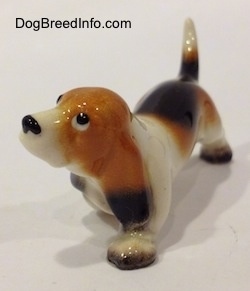 The front left side of a black, tan and white ceramic Basset Hound figurine. The paws of the figurine are lacking detail.