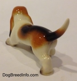 The back left side of a black, tan and white ceramic Basset Hound figurine. The tail of the figurine is arched up.