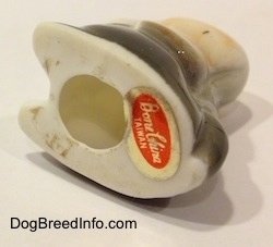The underside of a white with tan and black bone china Basset Hound puppy figurine. There is a hole and a sticker on the bottom of the figurine.
