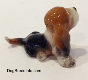 The right side of a black and brown with white ceramic Basset Hound figurine that is looking up. The figurine has finely detailed ears.