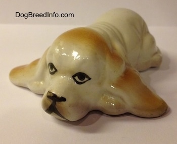 A white with tan porcelain Basset Hound figurine. The face of the figurine lacks detail.