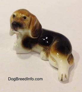 Topdown view of a Cute little black, brown and white porcelain Beagle figurine with two broken front legs. The figurine has a very detailed face.