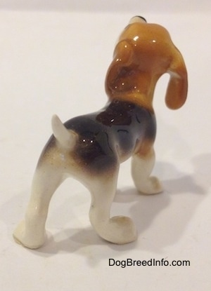 The back right side of a black and white with tan miniature Beagle figurine. The figurine has a short tail.