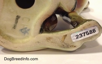 Close up - The underside of a black, brown and white porcelain Beagle figurine. There is a series of numbers, a hole and the word - Germany - on the underside of the figurine.
