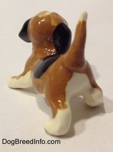 The back left side of a brown, black and white miniature Beagle in a crouching pose. The tail of the figurine is in the air.