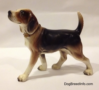 The left side of a black, brown and white ceramic Beagle figurine with a chain ID collar that reads "Beagle". The figurine has whisker dots on its muzzle.