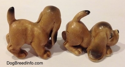 The right side of two Vintage miniature ceramic Bloodhound figurines. The paws of the figurines are detailed.
