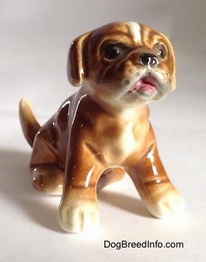 A brown with white Boxer puppy figurine that is in a sitting pose. The figurine has a very detailed face.