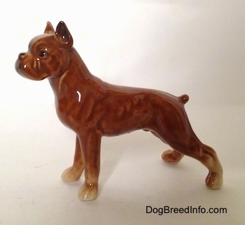 The left side of a porcelain brown Boxer dog figurine. The figurine has a short tail.