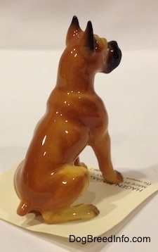 The back right side of a tan with black and white Boxer papa figurine. The figurine is very glossy.