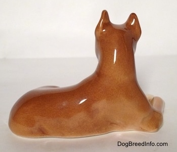 The right side of a brown with tan Boxer dog figurine in a laying down pose.