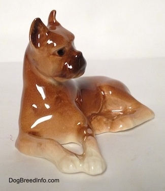 A brown with tan Boxer dog figurine in a laying down pose. The figurines front paws are attached.