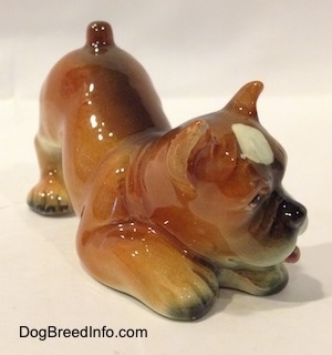 The front right side of a brown, black and white Boxer puppy figurine in a play bow pose.