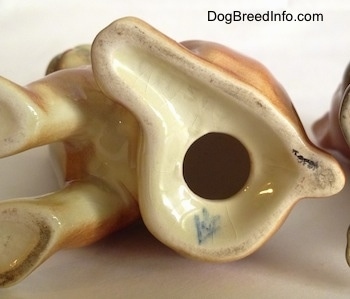 The underside of a brown with white and black Boxer puppy figurine. There is a hole in the bottom.
