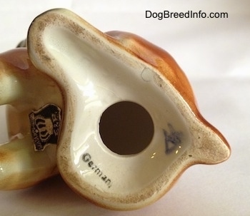 The underside of a brown with white and black boxer puppy figurine. There is a black and silver Golden Crown E & R Germany sticker on the belly of the figurine.
