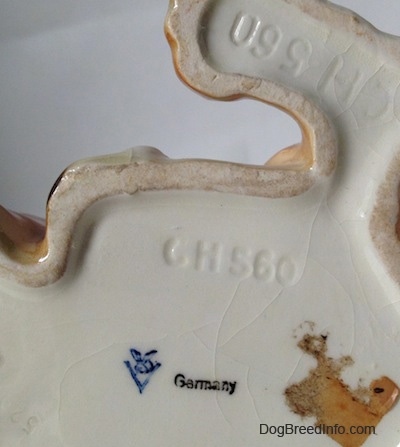 The underside of a fawn and white with black Boxer dog figurine in a laying pose. On the underside is the logo of Goebel Germany and above it is the number - CH560.