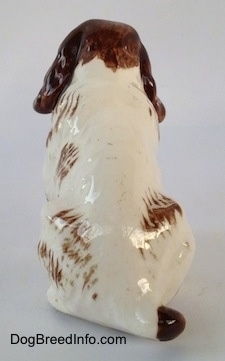 The back of a brown and white ceramic Brittany Spaniel that is in a sitting pose.