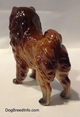 The back left side of a brown with black Chow Chow figurine. The figurine is glossy. Its tail is curled up over its back.