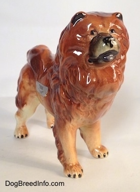 The front right side of a brown with tan and black Chow Chow figurine. The figurine has black eyes, inside ears and toe nails.