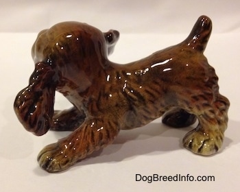 The left side view of a brown and tan Cocker Spaniel puppy figurine. The figurine has a short tail.