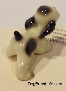The back right side of a white with black ceramic Cocker Spaniel puppy figurine. The figurine is very glossy.