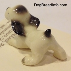 The back left side of a white with black ceramic Cocker Spaniel puppy figurine. The figurine has a short tail.