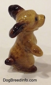 The right side of a tan with brown Cocker Spaniel figurine is sitting on its hind legs, it has its paws and ears out. It has very detailed hair brushings.