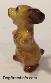 The left side of a tan with brown Cocker Spaniel figurine is sitting on its hind legs, it has its paws and ears out. The figurines mouth is open.
