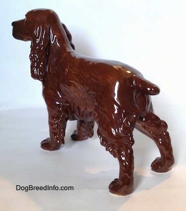 The back left side of a brown with black Cocker Spaniel porcelain figurine. Its hair is very defined. It has long ears that hang down to the sides.