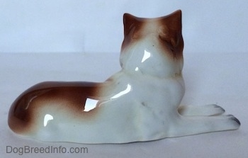 The right side of a figurine that is a brown and white Collie dog that is in a lying down pose. The figurine lacks fine details.