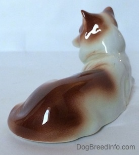 The back right side of a brown and white Collie dog figurine in a lying down pose. It is hard to tell the difference between the figurines body and its tail.