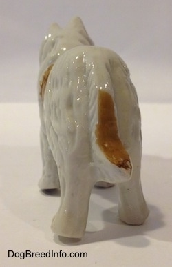 The back of a bone china figurine that is a white with tan Rough Collie. The figurines tail is connected to its body.