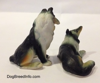 The back right side of two bone china figurines that are a sitting Rough Collie and a lying down Rough Collie.