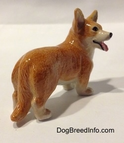 The back right side of a porcelain figurine that is a brown with white Cardigan Welsh Corgi dog in a standing pose. The figurine is glossy.