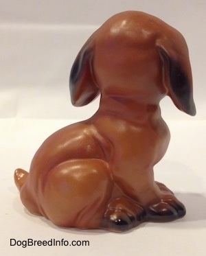 The left side of a brown with black Dachshund puppy in a sitting pose figurine. The figurine has body details.