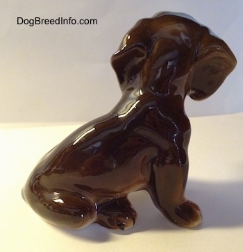 The right side of a brown with tan ceramic Dachshund figurine. The figurine has big ears and it has big paws.