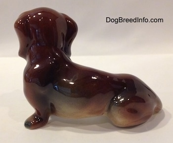 The left side of a figurine that is of a brown and black Dachshund in a sitting pose. The figurine is very glossy.