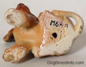 The underside of a brown with tan Dachshund puppy in a sitting pose figurine. The figurine has a hole in its bottom and above it is the number - M668 - stamped on it.