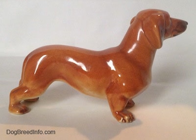 The right side of a figurine that is of a brown Dachshund in a standing pose. The paws of the figurine have great details.
