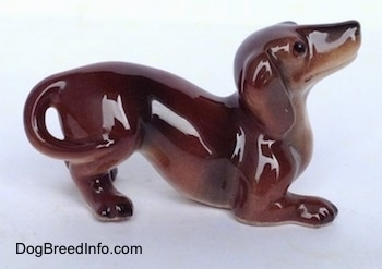 The right side of a brown with tan Dachshund figurine in a play bow pose. The tail of the figurine is attach to its leg.