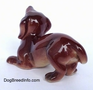 The back left side of a figurine that is a brown with tan Dachshund in a play bow pose. The figurines paws have fine details.