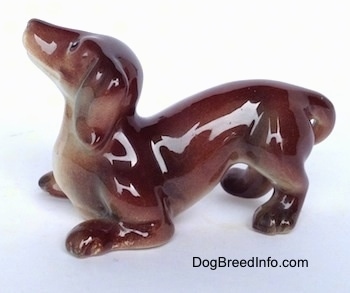 The left side of a brown with tan Dachshund figurine that is in a play bow pose. The figurines ears have great details.