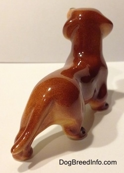 The bakc right side of a figurine of a brown Dachshund. The tail of the figurine is long and its attached to its back left leg.