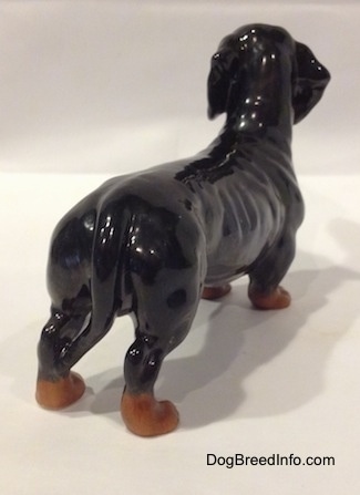The back right side of a black and brown Dachshund figurine. The figurine has a long tail.