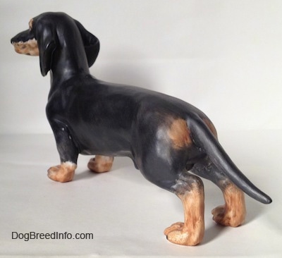 The back left side of a black with tan Dachshund figurine. The figurine has a slight gloss.