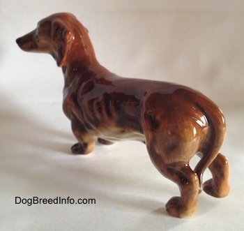 The back left side of a figurine of a brown Dachshund. The figurine has a long tail.