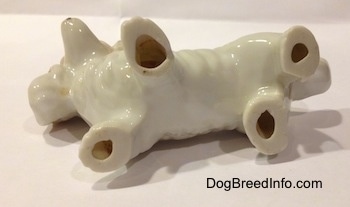 The underside of a porcelain white with tan long haired Dachshund figurine. The figurine has a holes in the bottom of every leg.